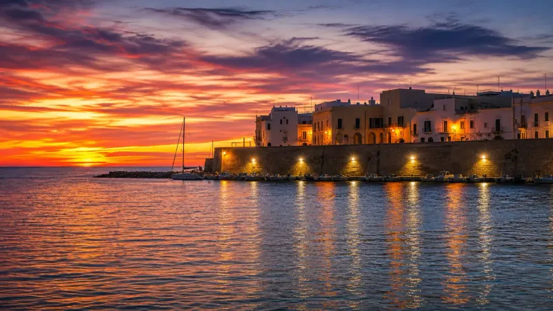 Il centro storico di Gallipoli al tramonto, con le luci sulle mura e le barche nel porto